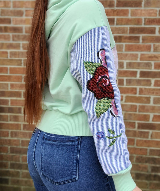 A woman wearing a green and pink embroidered hoodie.