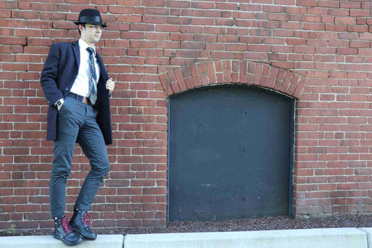 a man in a suit and hat leaning against a brick wall.