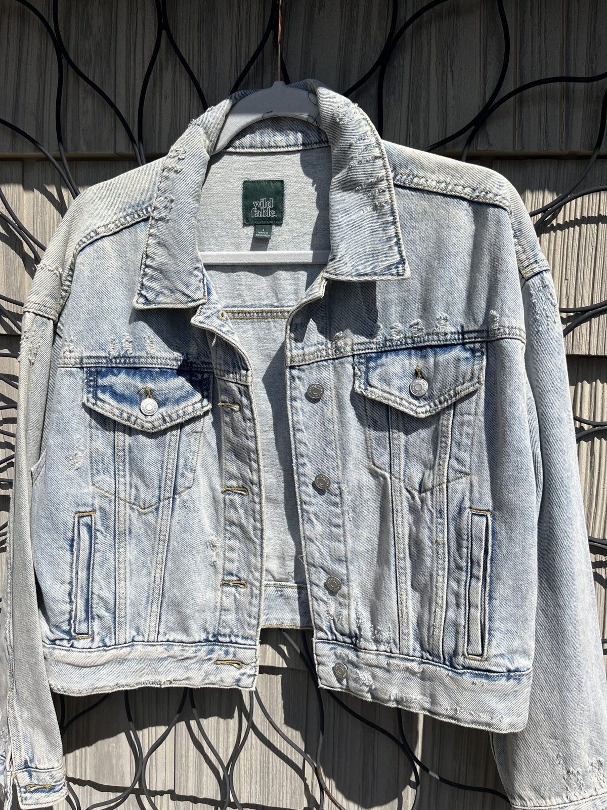 A light blue denim jacket hanging on a fence.