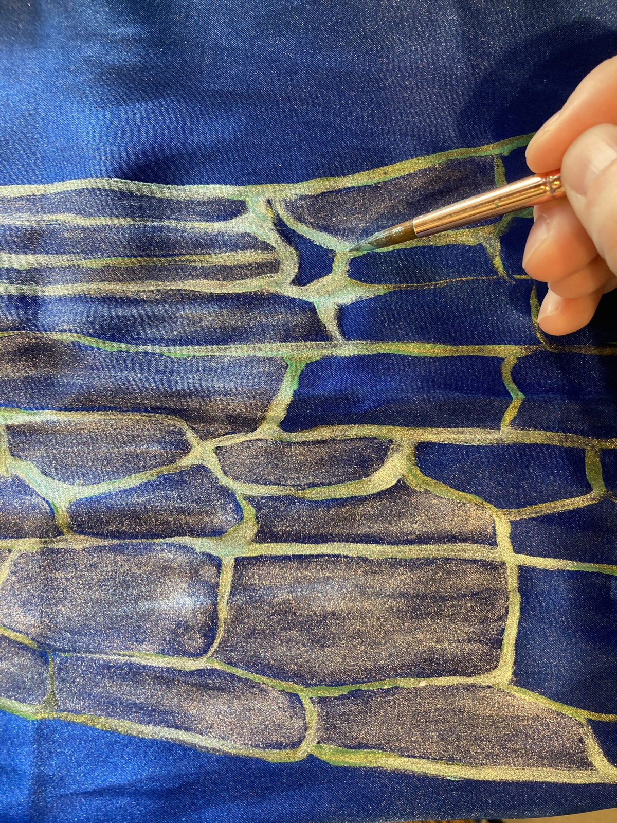 A person is drawing on a piece of paper while wearing their Hand-painted iridescent blue dragonfly wing scarf.