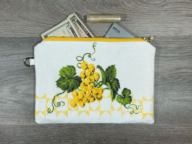 A white floral-patterned pouch with a zipper, containing money and a tube of lipstick, placed on a wooden surface.