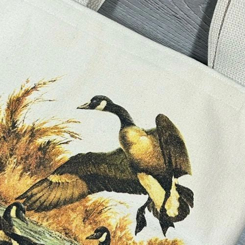 Image of a tote bag featuring a detailed illustration of a canada goose in a dynamic pose among tall grasses.