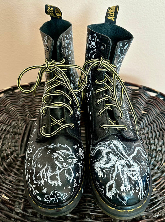 A pair of black dr martens boots with drawings on them.
