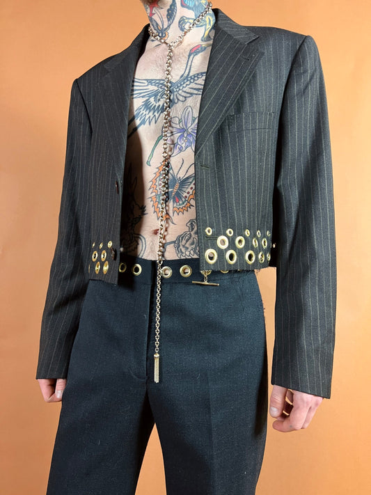 Tailored pinstripe jacket with unique metal grommet and chain detailing, paired with tattoos on display.
