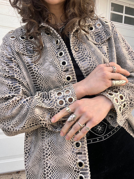 A person wearing a textured jacket with eyelet details, adorned with multiple rings on their fingers.