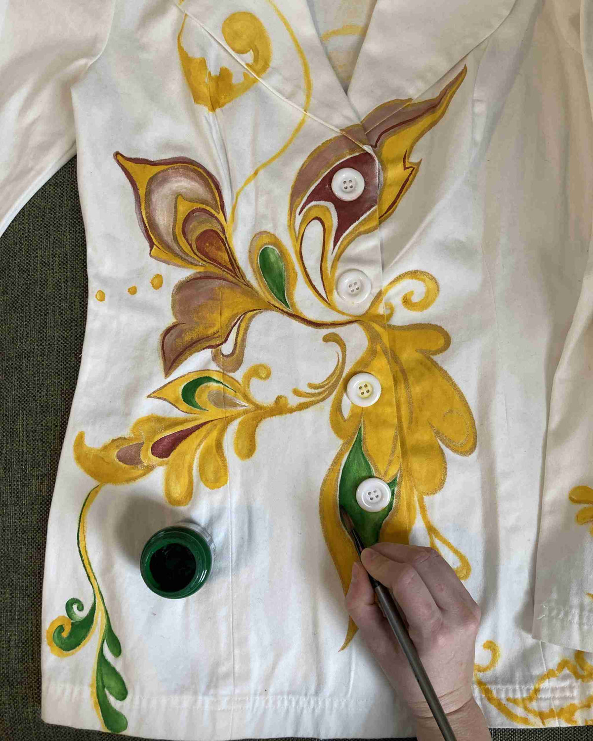 a person painting a white shirt with yellow and green designs.