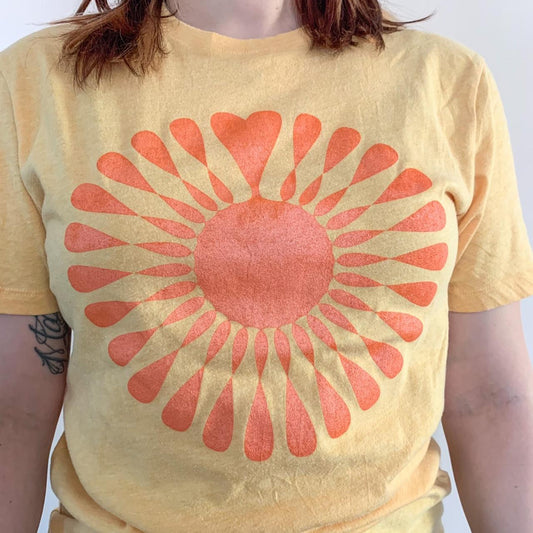 A woman wearing a yellow t - shirt with an orange sun on it.