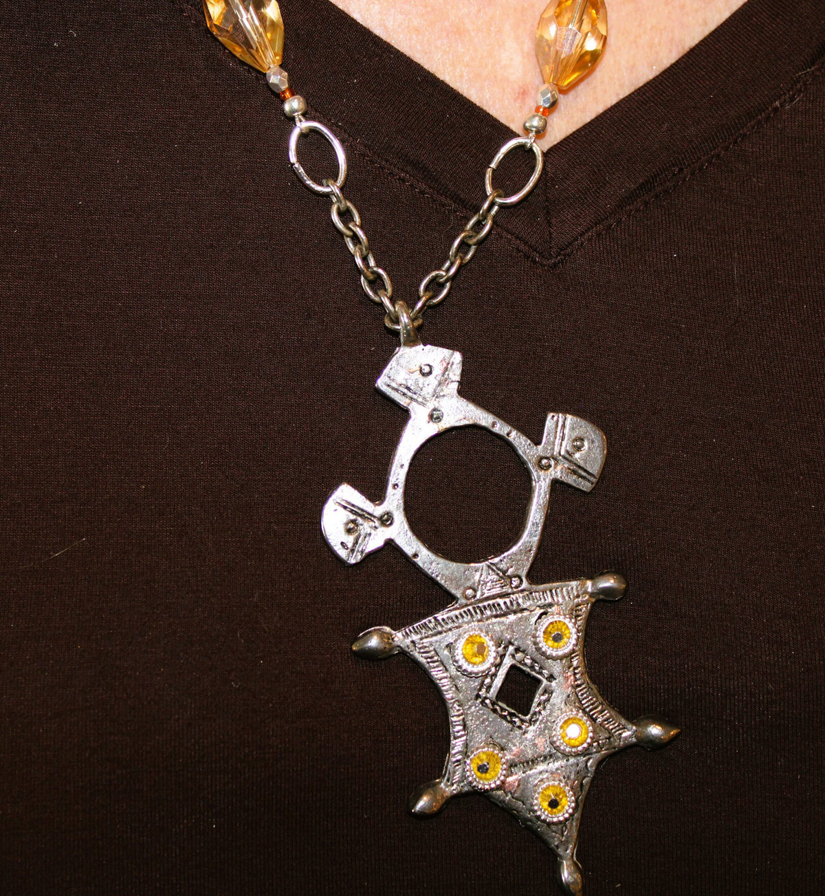 A woman wearing a necklace with a silver Aztec style pendant on it.