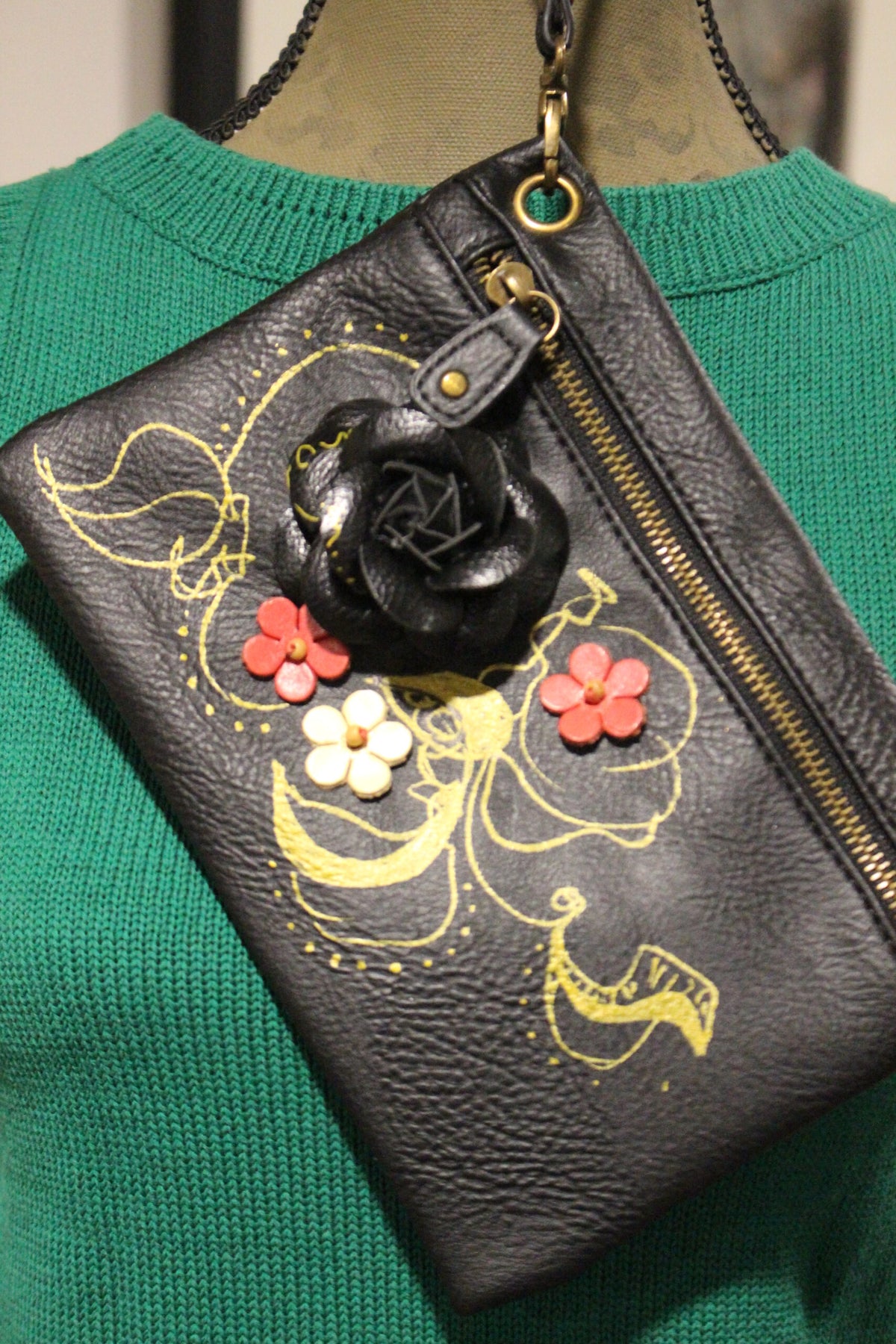 Green textured purse with floral design and a black charm hanging from the zipper.