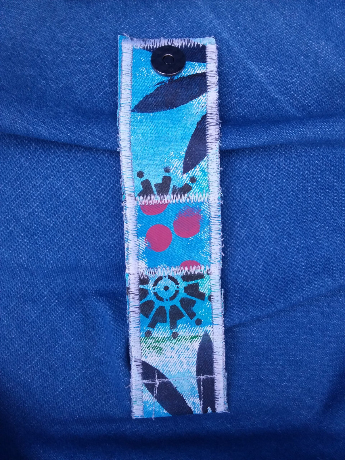 A hand painted, upcycled denim cuff with red dots and dark blue gears painted on it.