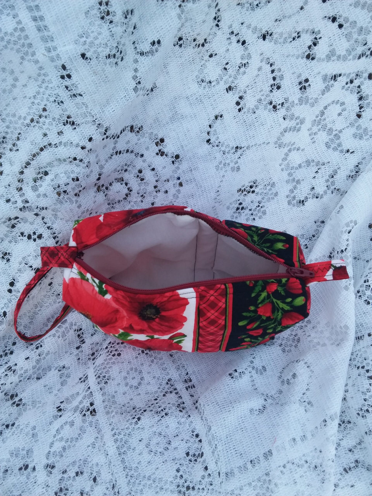 Bold poppy fabric, handcrafted into a quilted wristlet bag rests upon a vintage lace background.