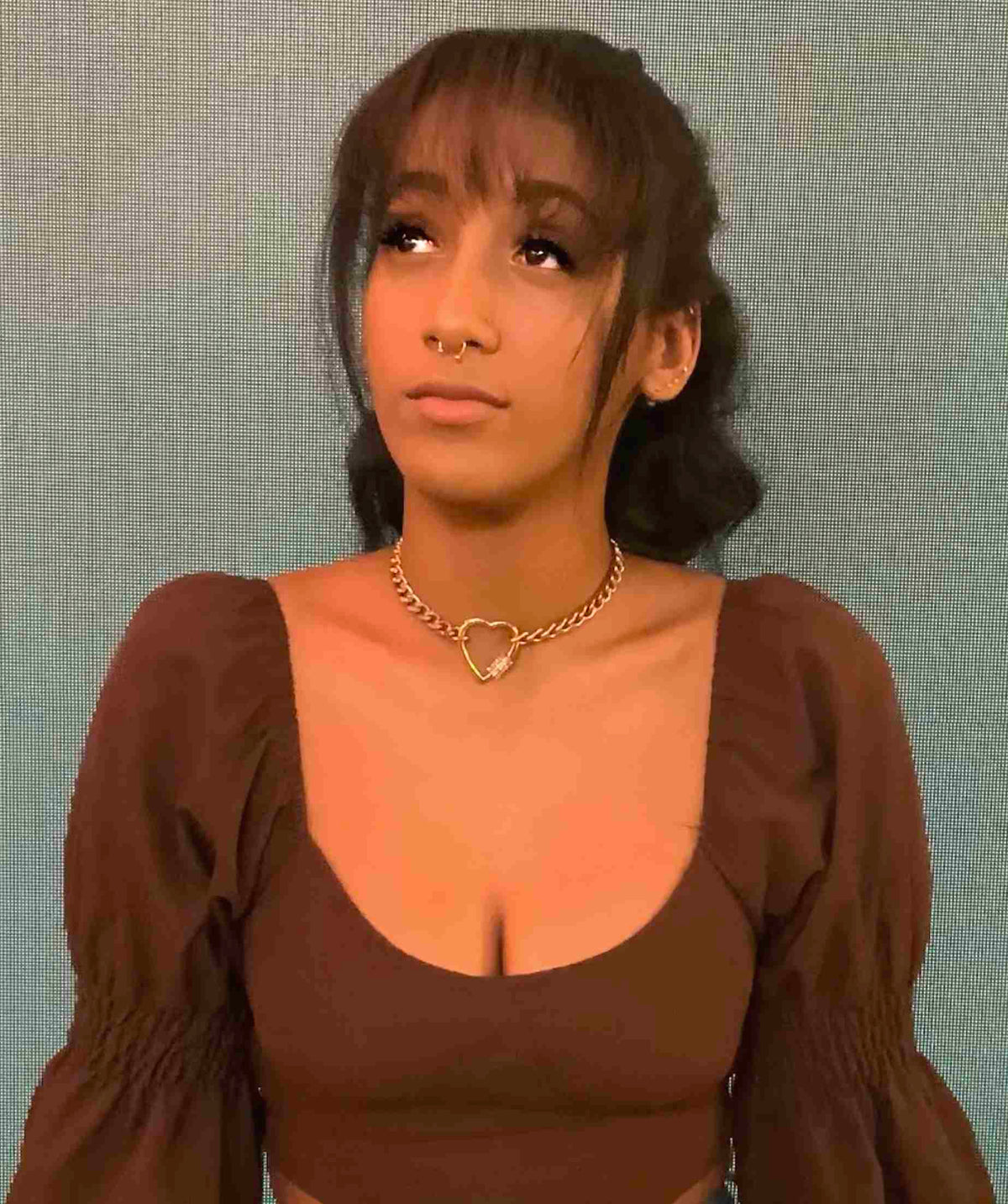 a woman wearing a brown top with a heart necklace.
