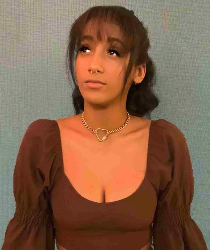 a woman wearing a brown top with a heart necklace.