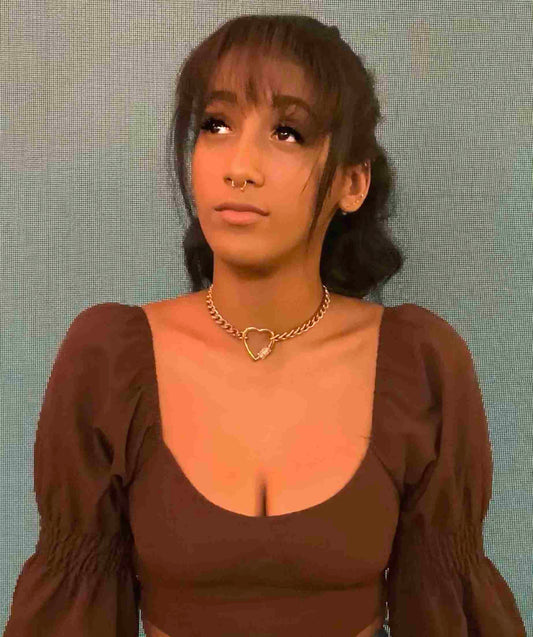 a woman wearing a brown top with a heart necklace.