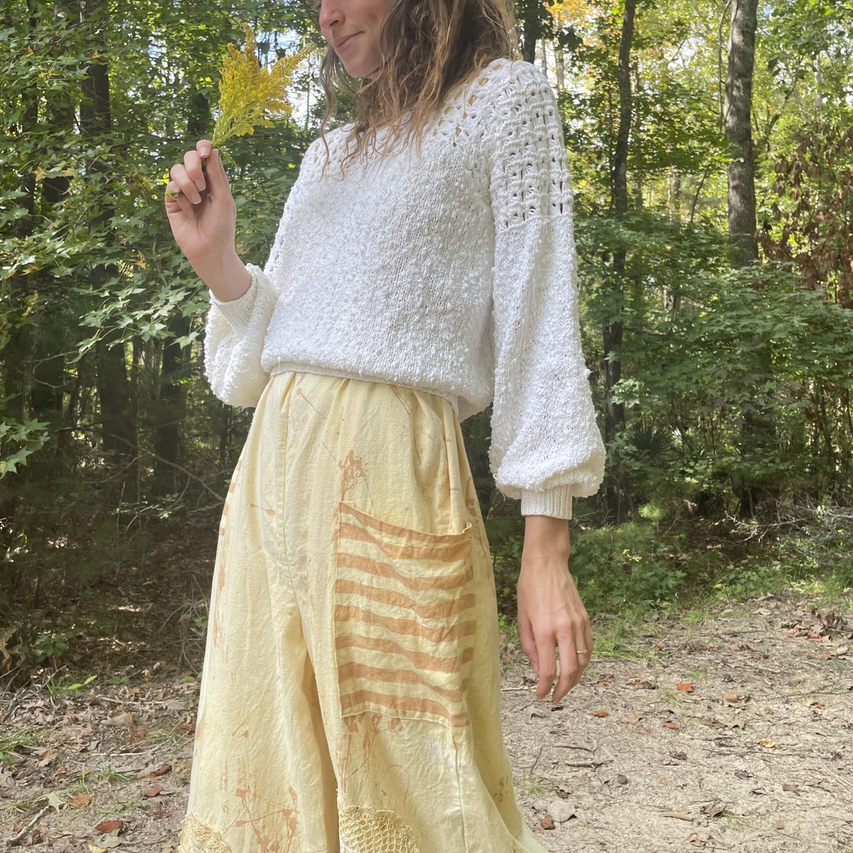 A woman is standing in the woods wearing a yellow skirt.