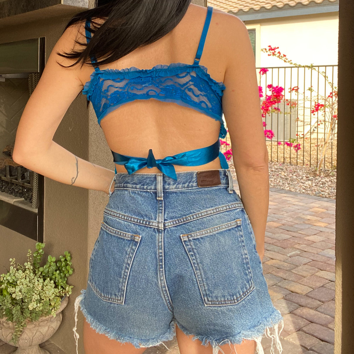 A woman wearing a 1of1 teal blue butterfly halter top and jean shorts.
