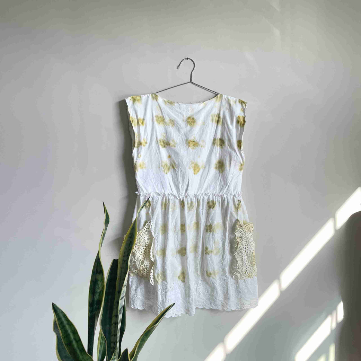 a white top hanging on a wall next to a potted plant.