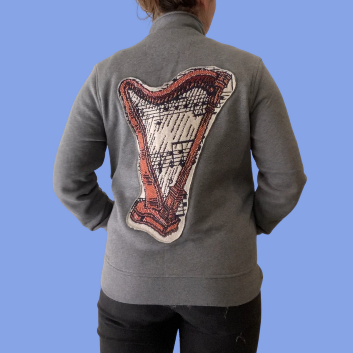 The back of a woman wearing a grey jacket with a harp on it.