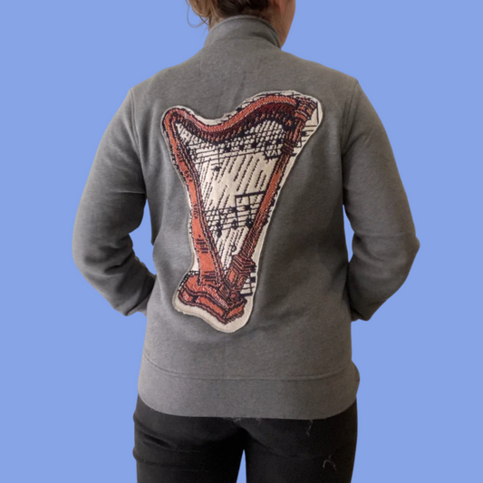 The back of a woman wearing a grey jacket with a harp on it.