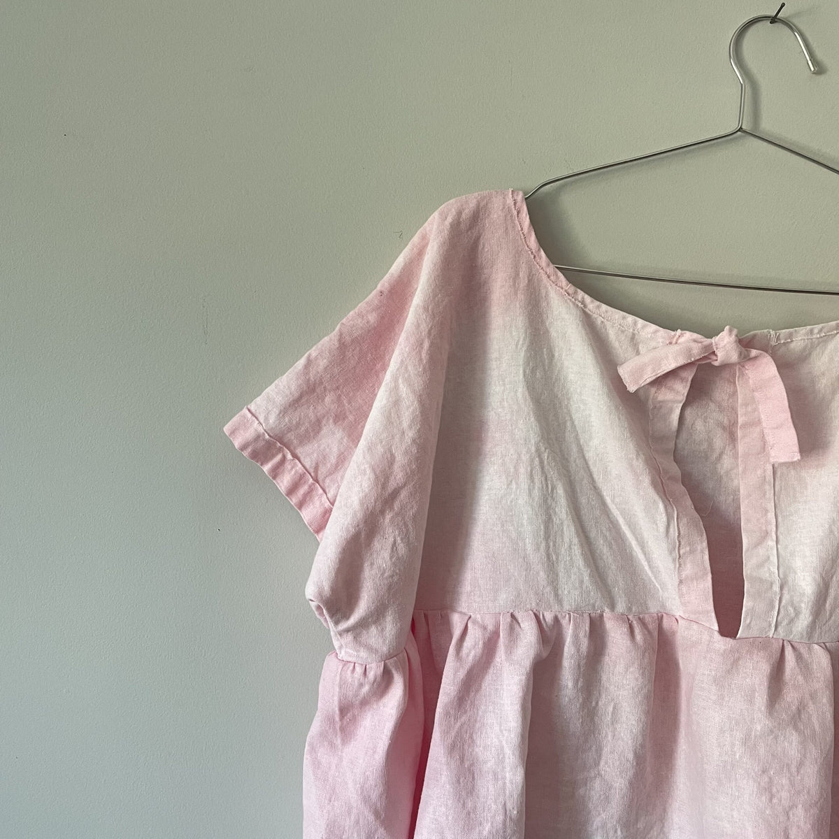 A pink blouse hanging on a hanger.
