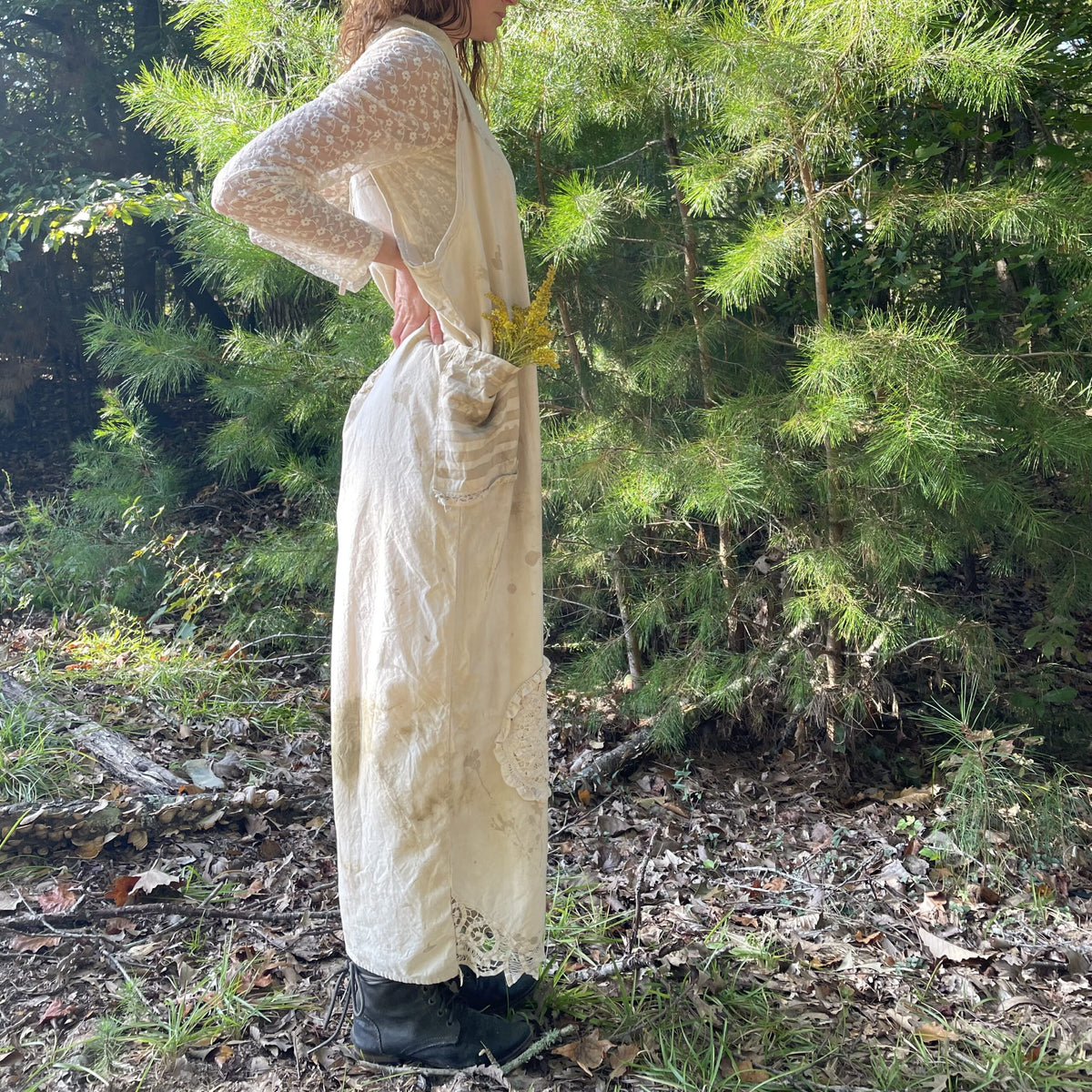 A woman is standing in the woods wearing a white dress.