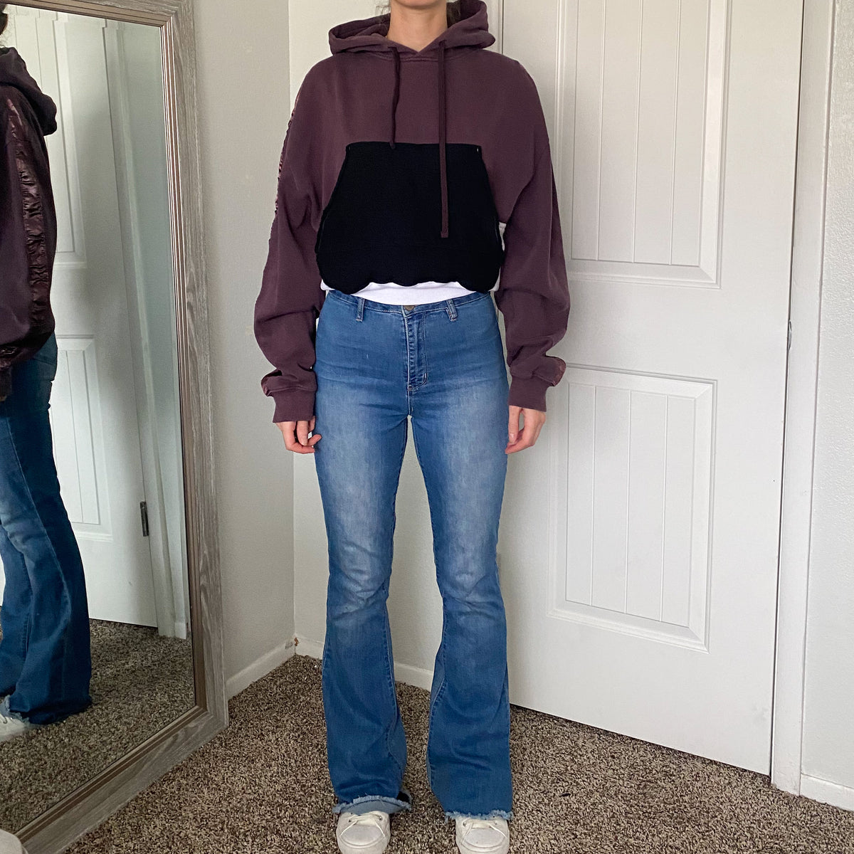 A woman wearing a purple hoodie and flared jeans.