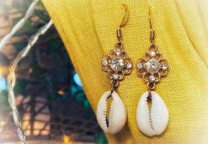 a pair of white and gold earrings sitting on top of a yellow cloth.