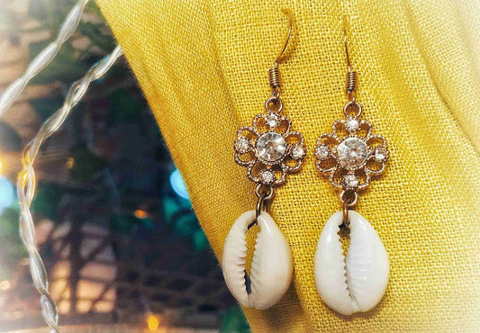 a pair of white and gold earrings sitting on top of a yellow cloth.