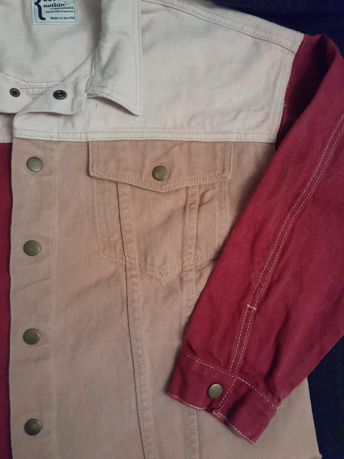 Skull & Flowers Frida Kahlo inspired pink color block denim jacket Large and a pair of jeans laying on a bed.