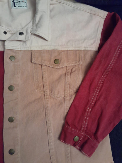 Skull & Flowers Frida Kahlo inspired pink color block denim jacket Large and a pair of jeans laying on a bed.