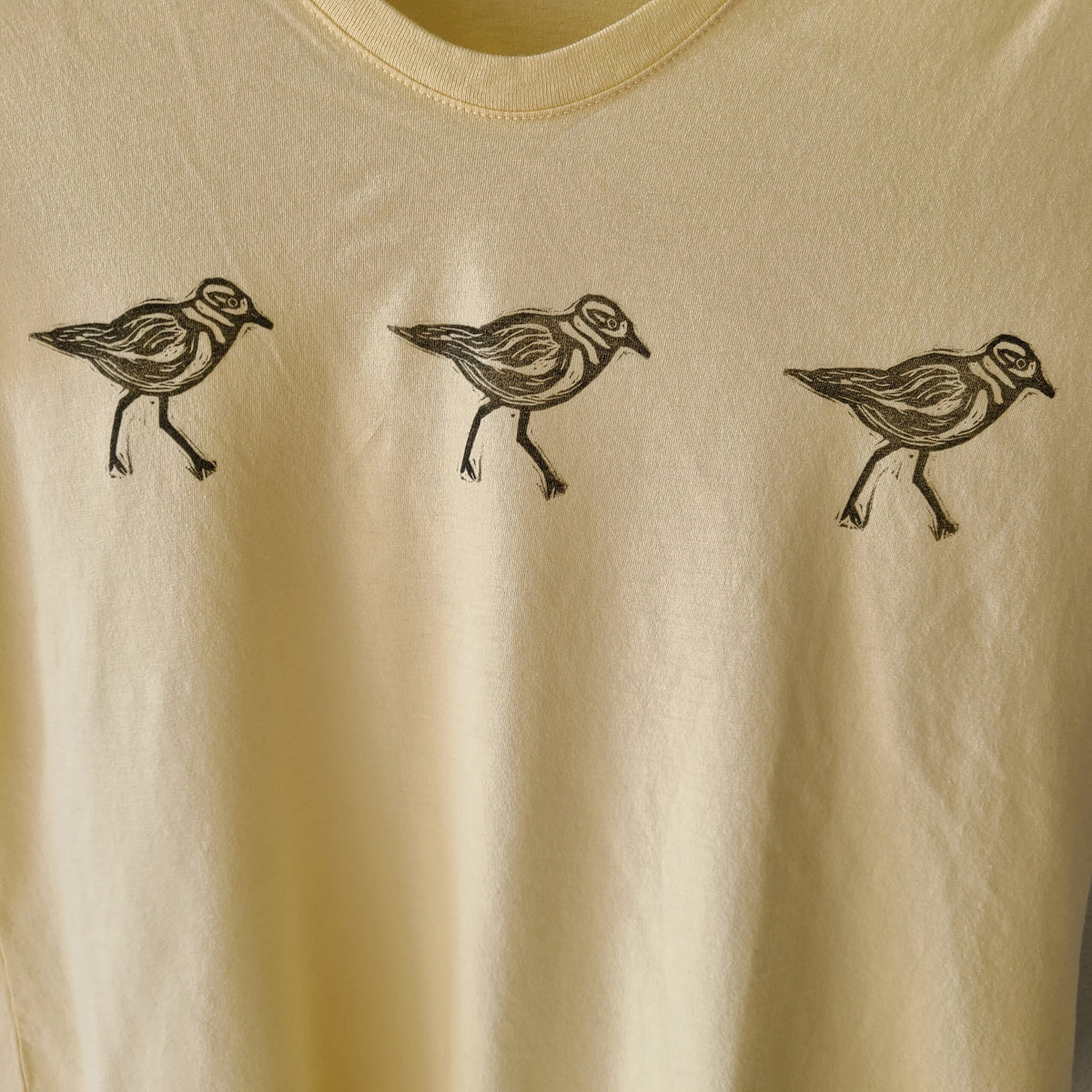 three birds on a yellow shirt with black ink.