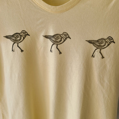 three birds on a yellow shirt with black ink.