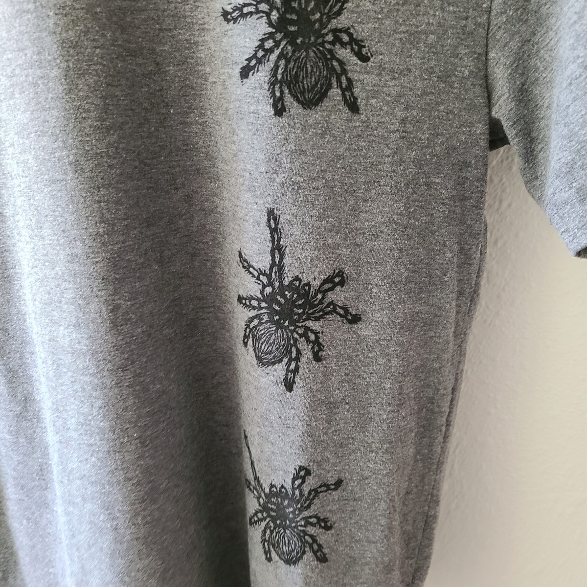 a gray t - shirt with black spiders on it.