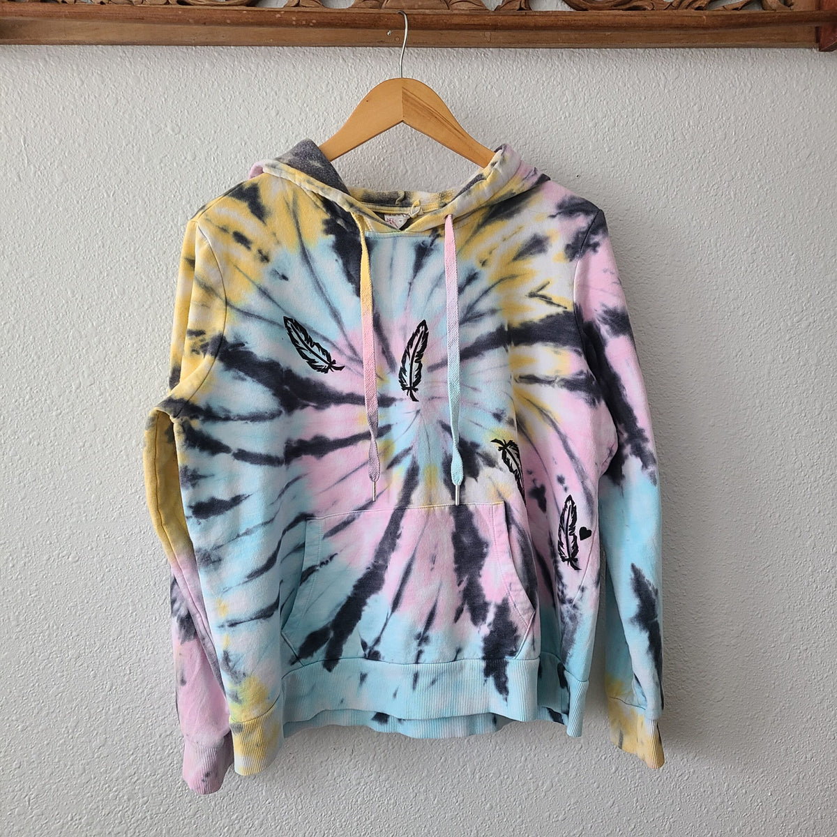 A tie dye hoodie hanging on a wooden hanger.