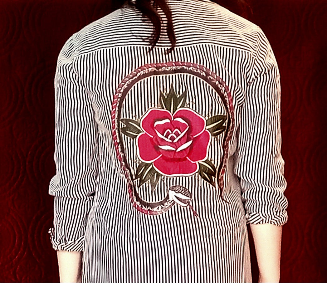 The back of a woman wearing a shirt with a rose embroidered on it.