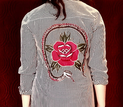 The back of a woman wearing a shirt with a rose embroidered on it.