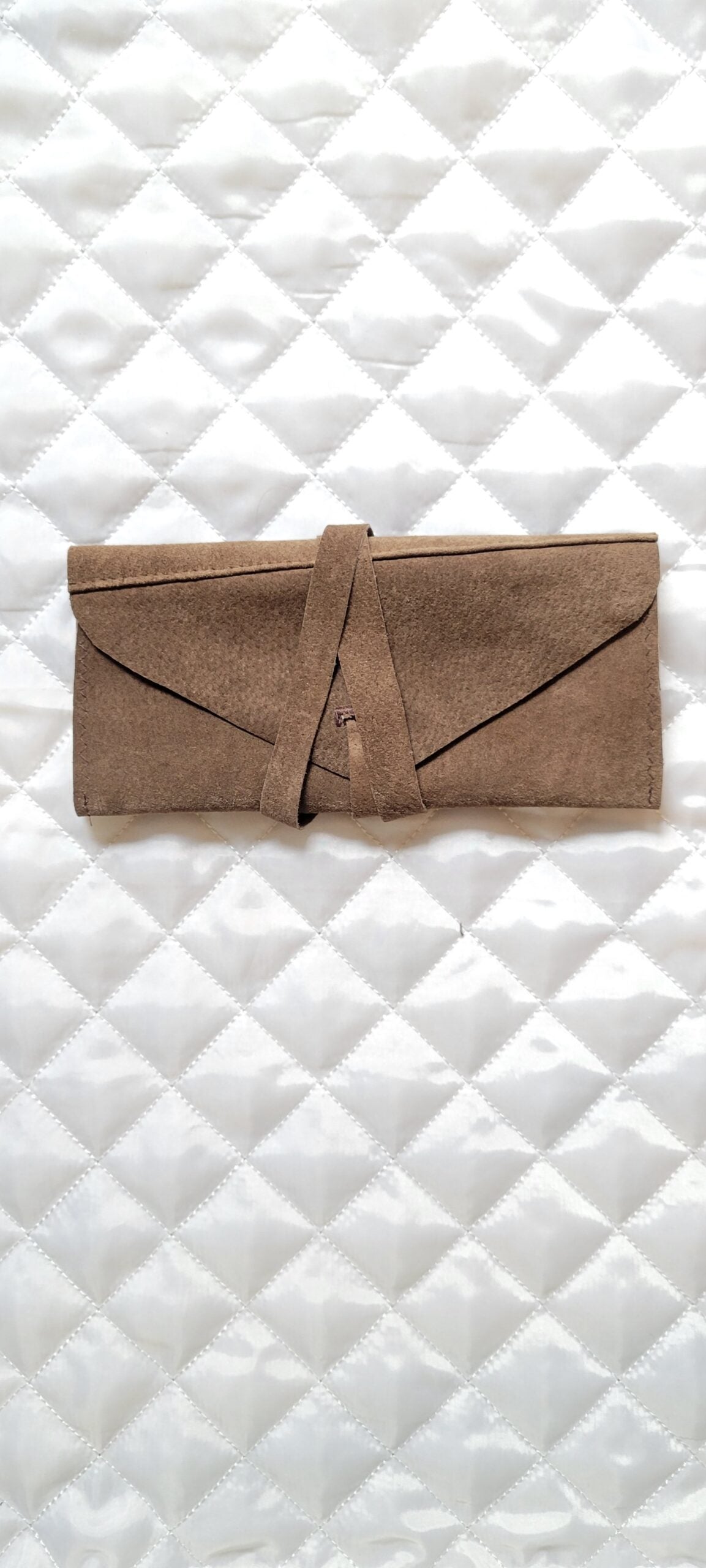 A brown leather pouch on a white quilted surface.