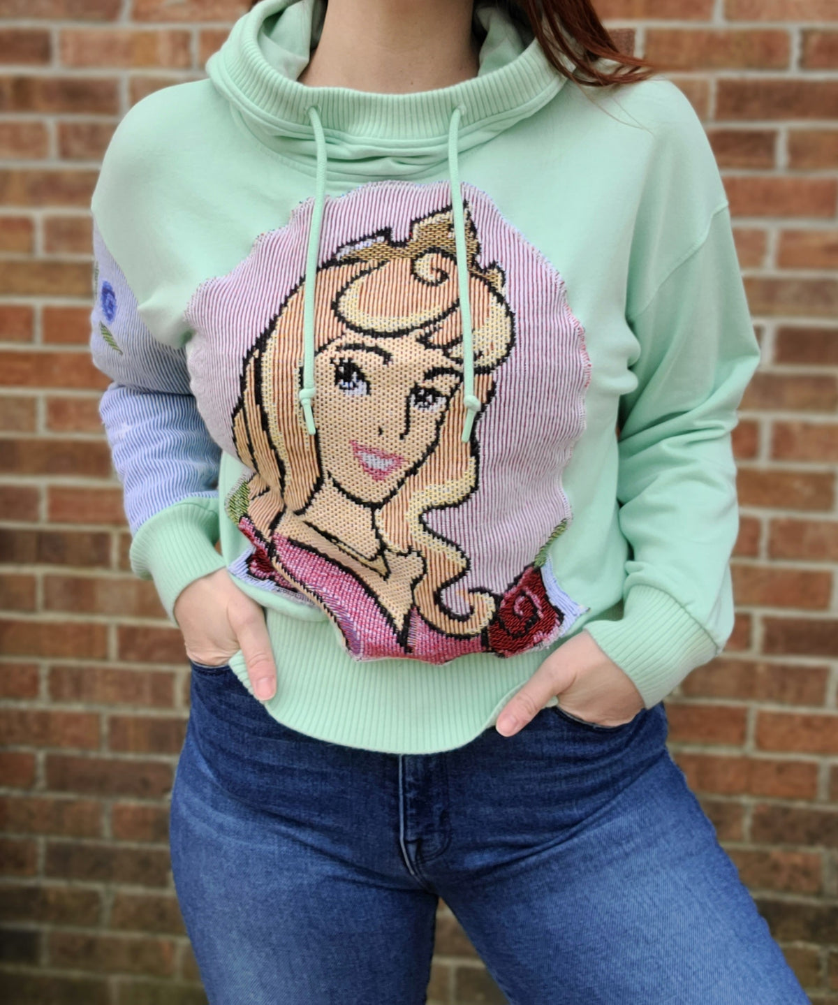 A woman wearing a green hoodie with a disney princess on it.