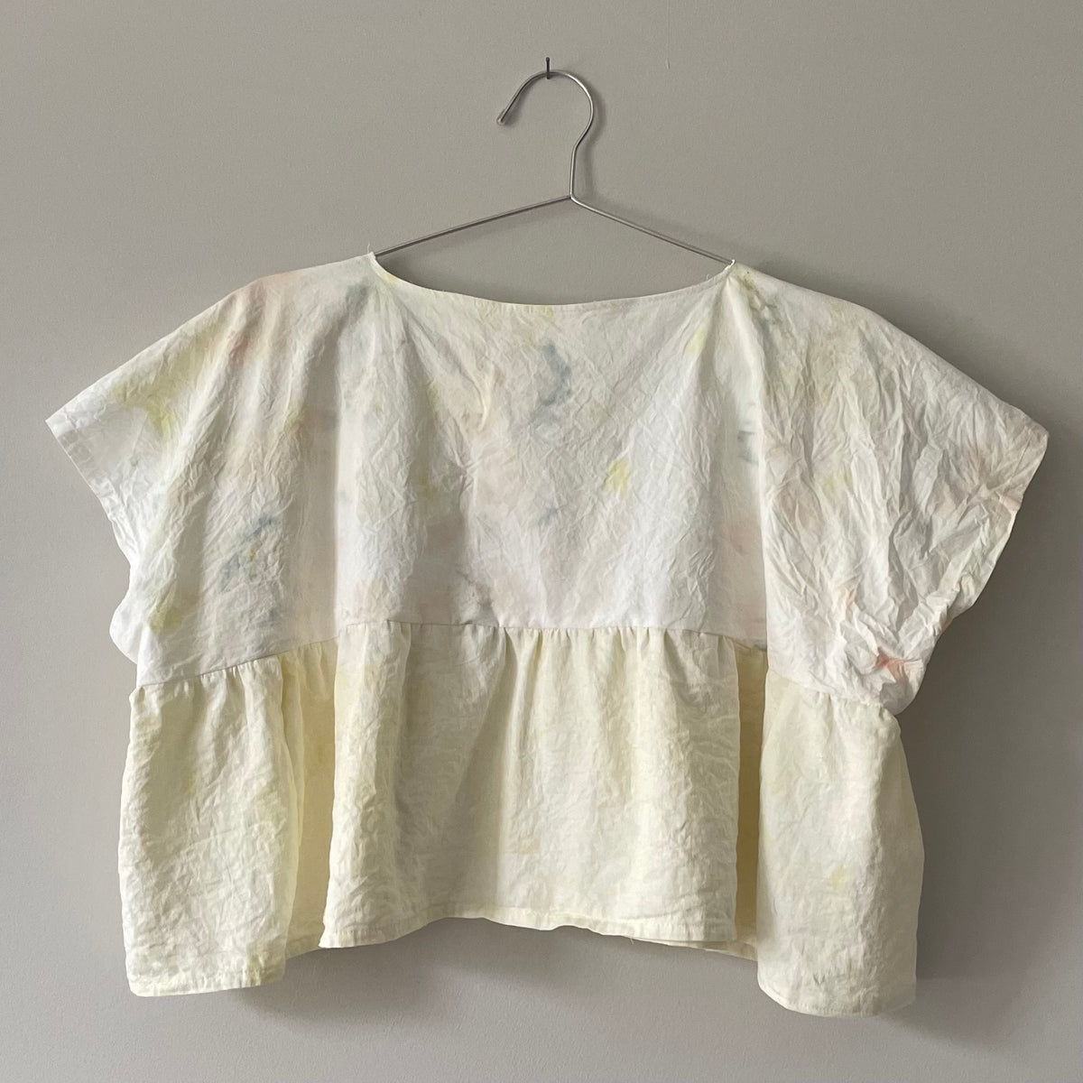 A Yellow Tie-dyed Babydoll Crop Top hanging on a hanger.