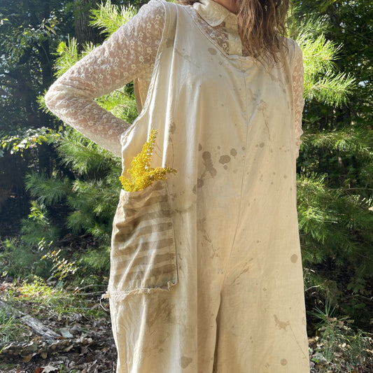A woman is standing in the woods wearing a white overall.