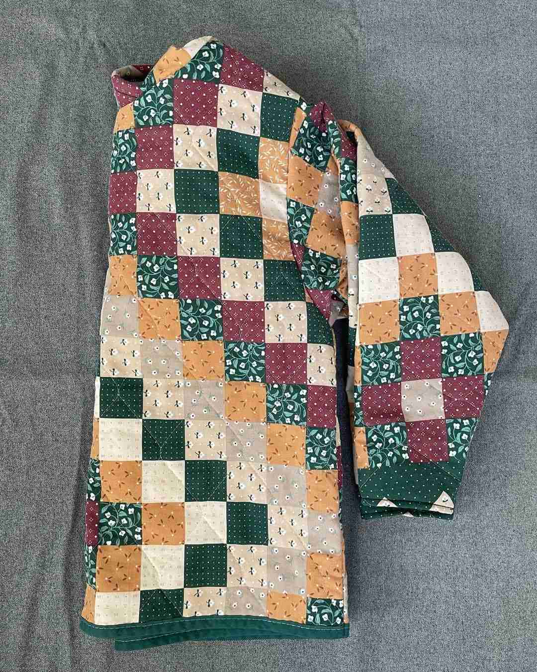a green, yellow, and red patchwork jacket laying on a bed.