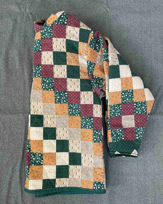 a green, yellow, and red patchwork jacket laying on a bed.