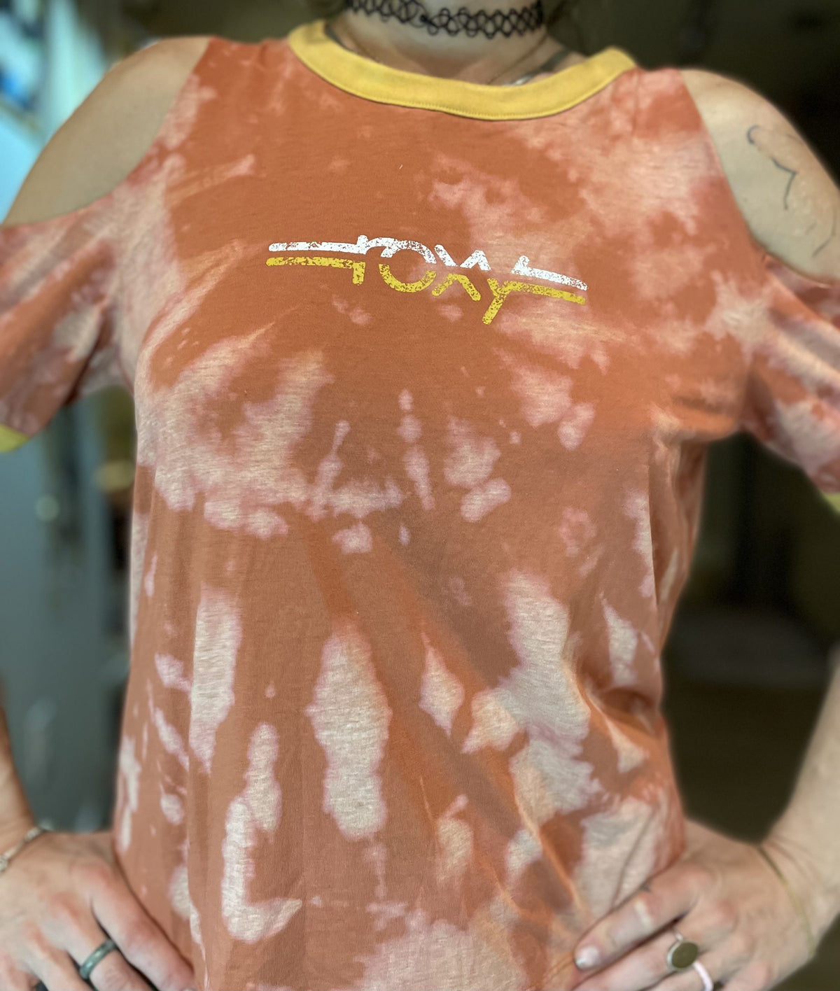 A woman wearing the Roxy tie dye cut-out tee with a yellow stripe around her neck.