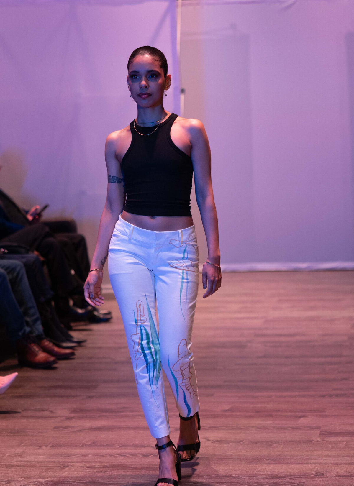 a woman walking down a runway wearing white pants.