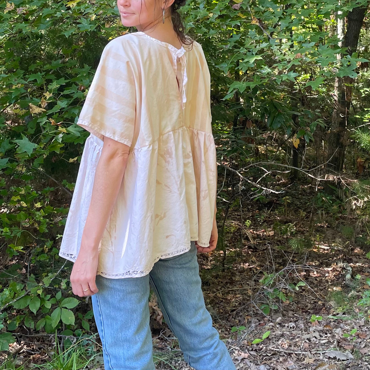 A woman is standing in the woods wearing jeans and a blouse.