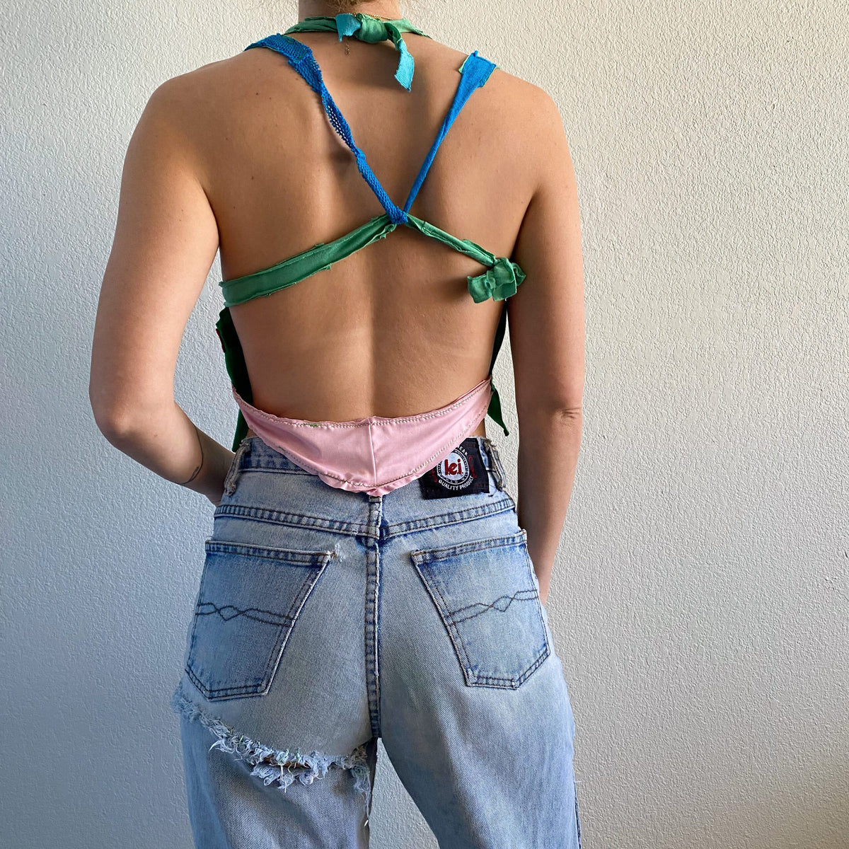 A woman wearing a 1of1 watermelon cross back halter top and blue jeans.