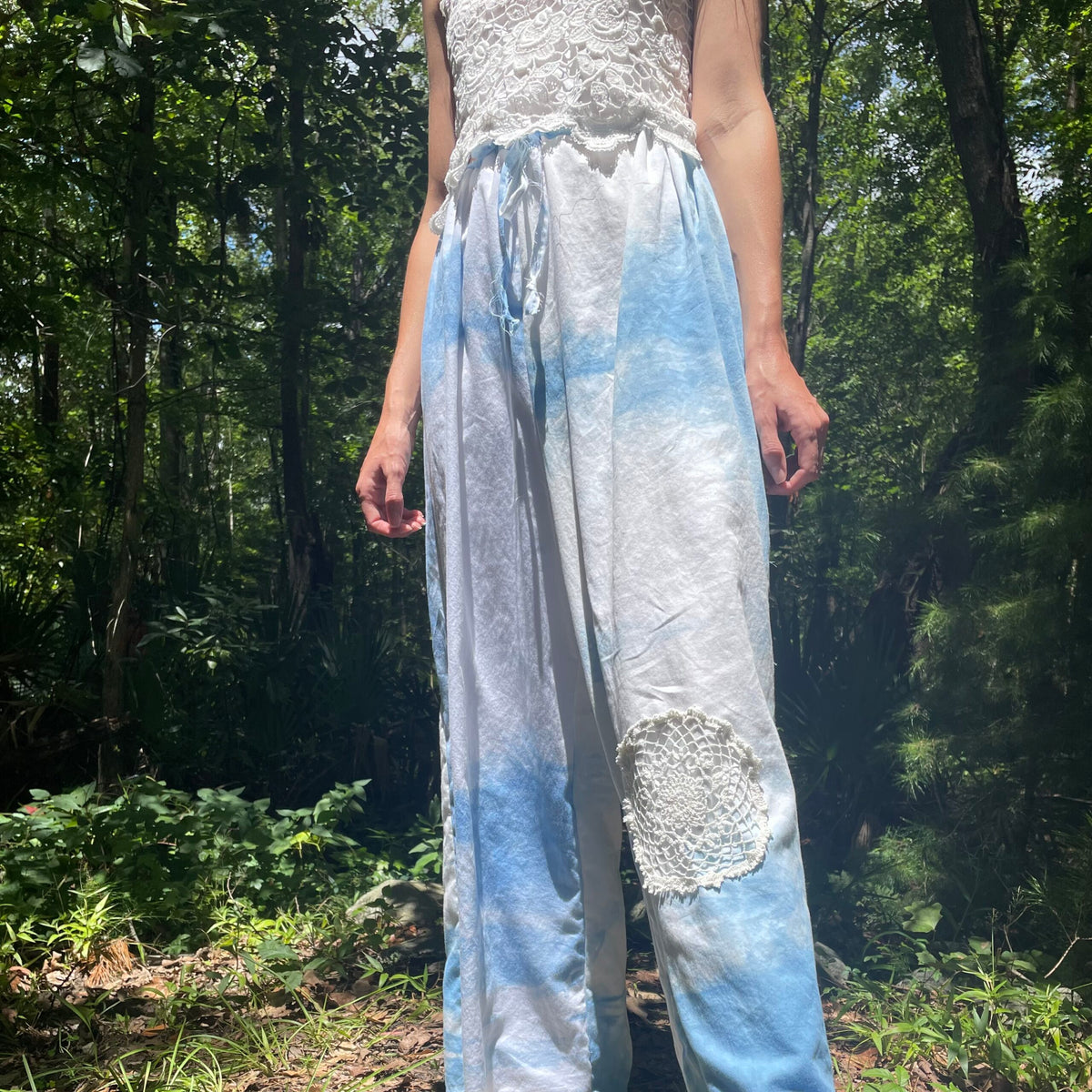 A woman is standing in the woods wearing indigo tie dyed pants.