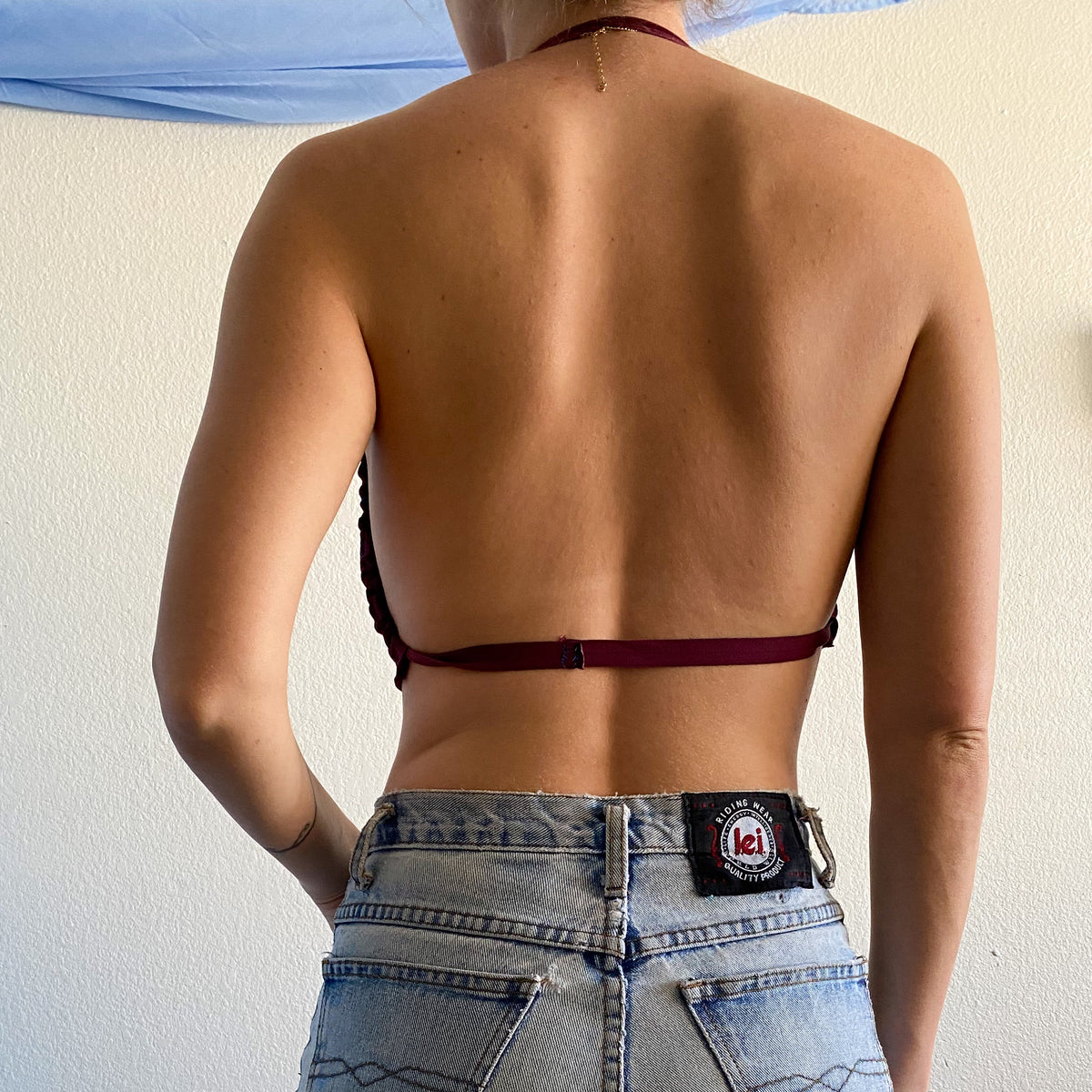 A woman in a 1of1 painted text print maroon halter crop top is standing back to back.