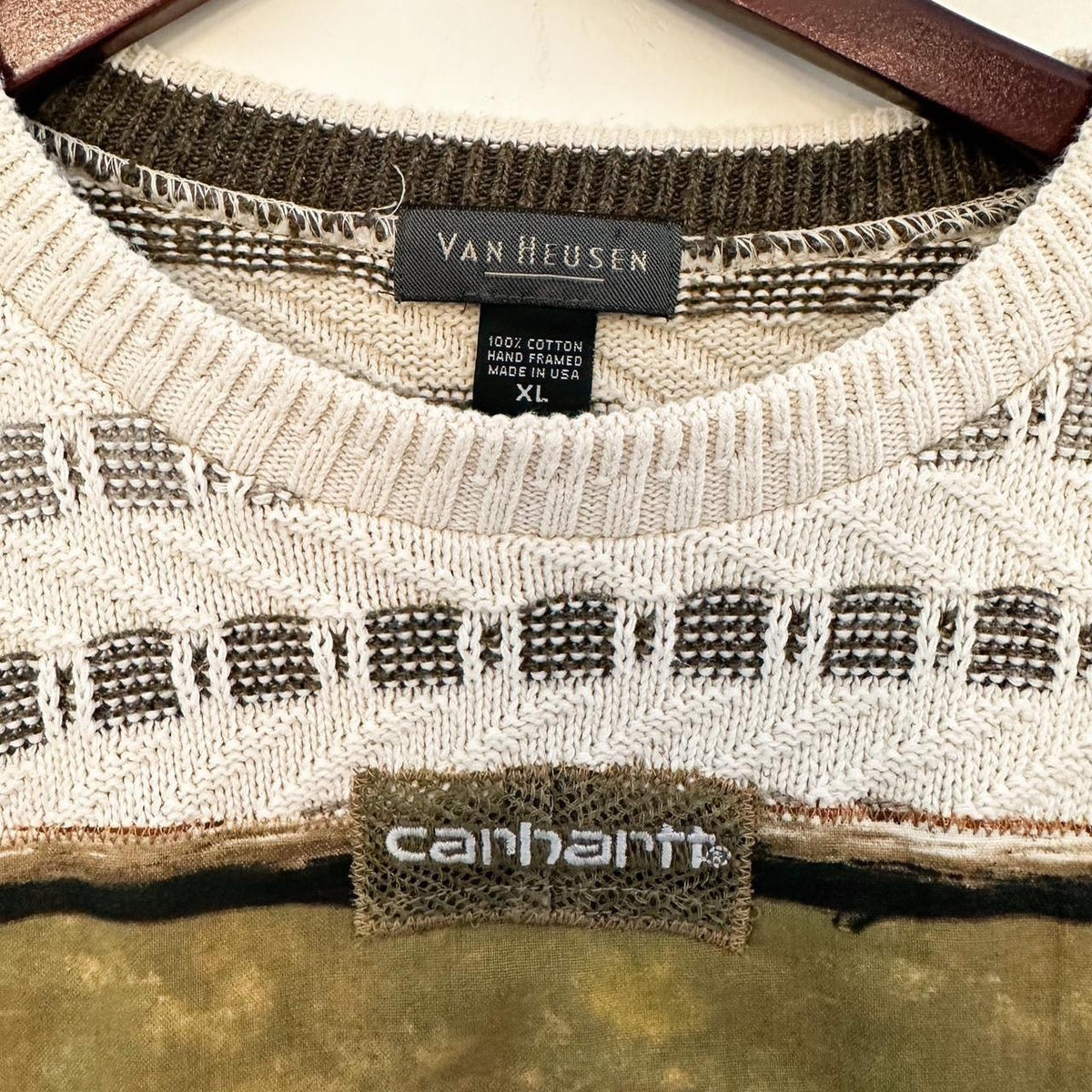A Neutral Duck & Carhartt Grandpa Sweater Rework hanging on a hanger on a wall.