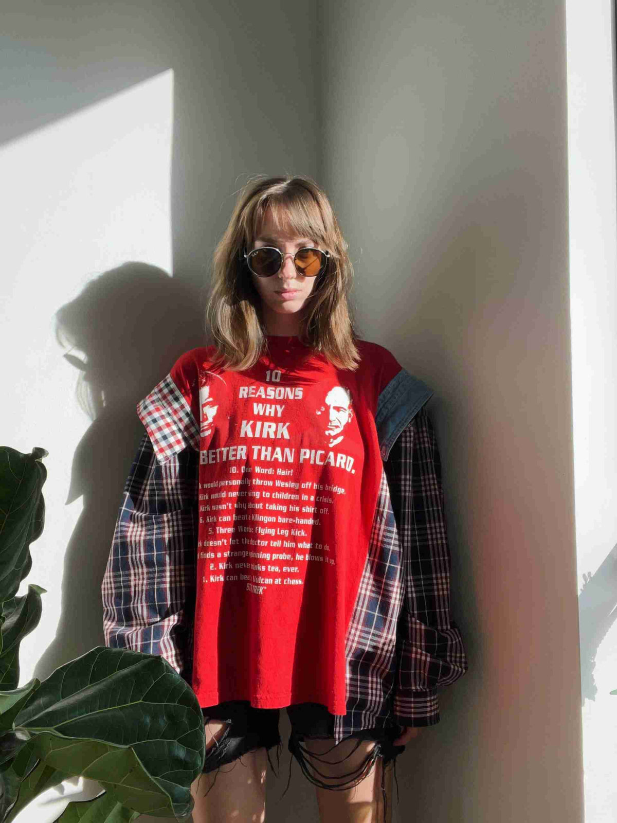 a woman standing against a wall wearing a red shirt.